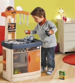Jouets : pour garçon, ustensiles de cuisine Un petit garçon est penché sur une casserole posée sur une cuisinière proportionnée à sa taille. Il tient le couvercle de la casserole dans la main gauche et une cuillère dans la droite, pour goûter sa préparation semble-t-il.