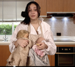 Une jeune fille, l'air épuisée, avec deux poupons/bébés dans les bras dans sa cuisine