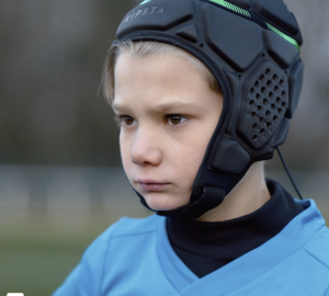 un petit garçon, visage fermé, casque de rugby sur la tête