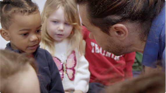 Deux enfants de maternelle, un adulte penche vers eux.